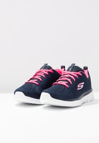 Jūras spēku sporta apavi ar rozā šņorēm, teksturētu acu augšdaļu, baltu zoli un logotipu sānos; izstrādāti komfortam un atbalstam.