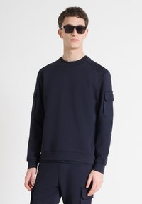 Sudadera azul marino con cuello redondo, que cuenta con dos bolsillos tipo parche en las mangas y un detalle texturizado en los hombros.