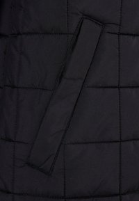 Čierna prešívaná puffer bunda so hladkou textúrou, s obdĺžnikovými panelmi a postranným uchom pre jednoduché nosenie.
