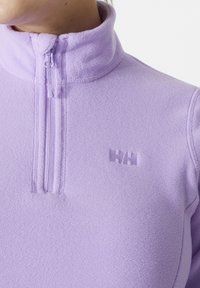 Jasnofioletowy polarowy półgolf z zamkiem błyskawicznym, z wysokim kołnierzem, z haftowanym logo na piersi. Miękka tekstura, bez wzorów.