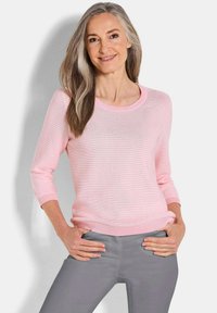 Hellrosa gestreifter Pullover mit Dreiviertelärmeln und rundem Ausschnitt, kombiniert mit grauen Hosen. Weiche Textur und lässige Passform.
