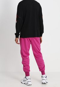 Mustapaita pitkillä hihoilla, joissa on graafisia yksityiskohtia hihoissa, yhdistettynä vaaleanpunaisiin trikootyylisiin housuihin, joissa on elastiset hihnat ja valkoiset urheilukengät.