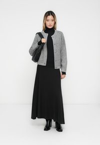Šedý pletený cardigan s knoflíky, černý rolák a černá maxi sukně; modelka nese černou kabelku a má na sobě černé kotníkové boty.