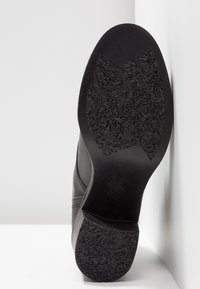 Chaussure en cuir noir avec semelle extérieure en caoutchouc texturé, dotée d'un petit talon, d'une tige lisse et de coutures discrètes sur les côtés.