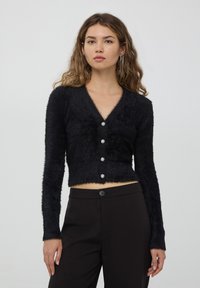 Cardigan nero cropped realizzato in materiale morbido e peloso, con un profondo scollo a V e cinque bottoni decorativi con un design floreale.