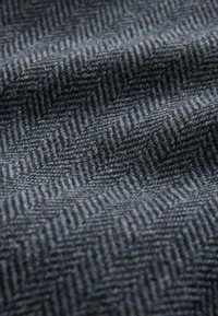 Gewebter Stoff in einem dunkelblauen und grauen Fischgrätenmuster, mit einer strukturierten Oberfläche und einem weichen, wolartigen Erscheinungsbild.