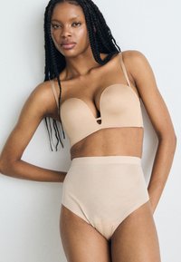 Nude padded bh met een diep decolleté en dunne verstelbare bandjes, gecombineerd met hooggeknoopte, naadloze nude slipjes, beide glad en aansluitend.