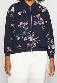 Giacca da bombardiere navy con motivo floreale in rosa e bianco, presenta una zip frontale e polsini a coste. Tessuto morbido con una vestibilità rilassata.