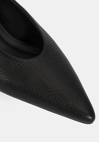 Chaussure à talon haut en cuir noir avec un bout pointu et une texture lisse, présentant un design découpé élégant sur les côtés.