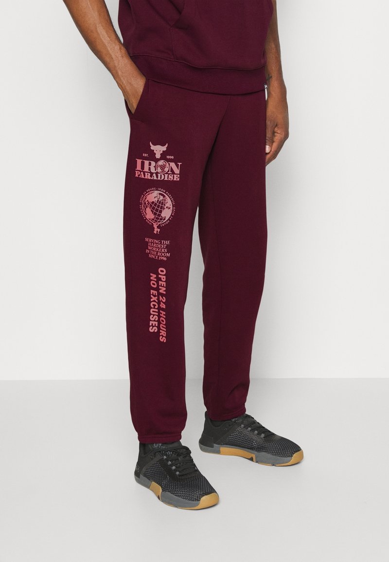 Pantalones jogger burdeos con gráficos impresos en rosa, que cuentan con bolsillos, cinturilla elástica y puños, combinados con zapatillas deportivas negras.
