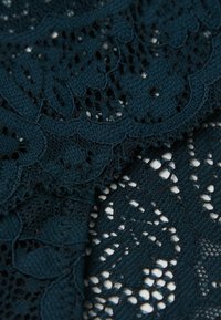 Ciemnozielona koronkowa tkanina z misternymi kwiatowymi i geometrycznymi wzorami, o zróżnicowanej teksturze i otwartości w całym projekcie.