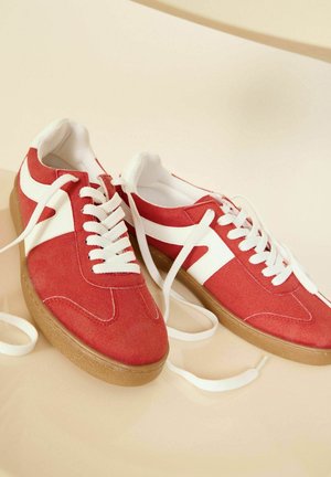Rode suède sneakers met witte accenten, met een klassieke vetersluiting en een getextureerde gumzool. De veters zijn losgeknoopt en plat neergelegd.