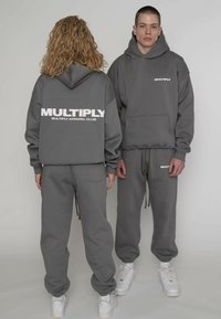 Grau melierter Kapuzenpullover und Jogginghose mit großem weißem "MULTIPLY"-Logo auf Vorder- und Rückseite, mit Taschen und gerippten Bündchen.