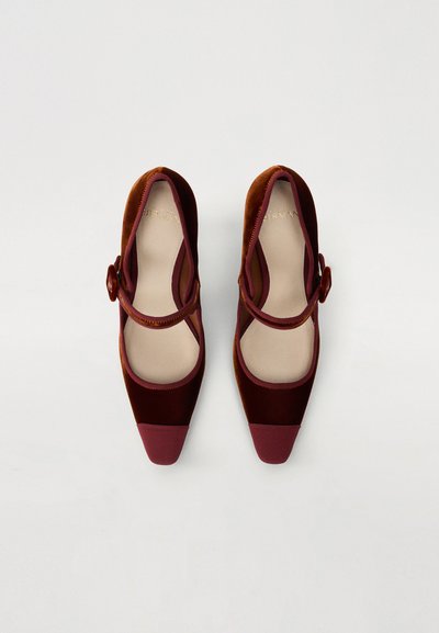 Chaussures Mary Jane en velours bordeaux avec un bout pointu, une épaisse lanière et un détail de bouton rond. Semelle en caoutchouc rouge contrastant avec un motif texturé.