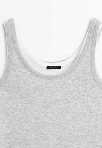 Close-up van twee mouwloze geribbelde tanktops, één lichtgrijs gedragen over een witte, met ronde halslijnen en een merklabel aan de binnenkant van de kraag.