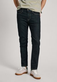 Tummat farkut slim-fit-mallissa, joissa on klassinen viiden taskun muotoilu ja kontrastien ompelu. Yhdistetty valkoisiin lenkkareihin.