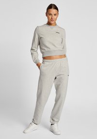 Ljust grå matchande sweatshirt och sweatpants-set, med ribbad nederkant, långa ärmar och logotypdetalj. Tillverkad av mjukt bomullsblandat material.