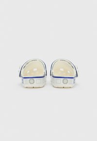 Beli in modri natikači brez pet, zasnovani z robotskimi detajli, prikazani s hrbtne strani na enobarvni beli podlagi.