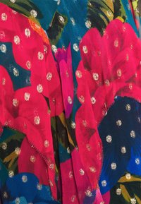 Pestrý šátek s velkými růžovými a modrými květinovými vzory a metalickými zlatými tečkami na tmavém pozadí, vyrobený z lehké texturované tkaniny.