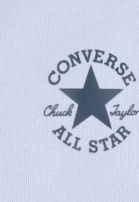 Hele sinine kangas, millel on must täht, millel on tekst "CONVERSE" ja "ALL STAR" ning kõveras kujunduses "Chuck Taylor".