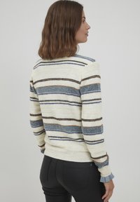 Adīta džemperis krēmkrāsā ar ziliem, brūniem un oranžiem svītrainiem. Ar ribotām piedurknēm un apakšmalu, mīkstu tekstūru un brīvu piegriezumu.