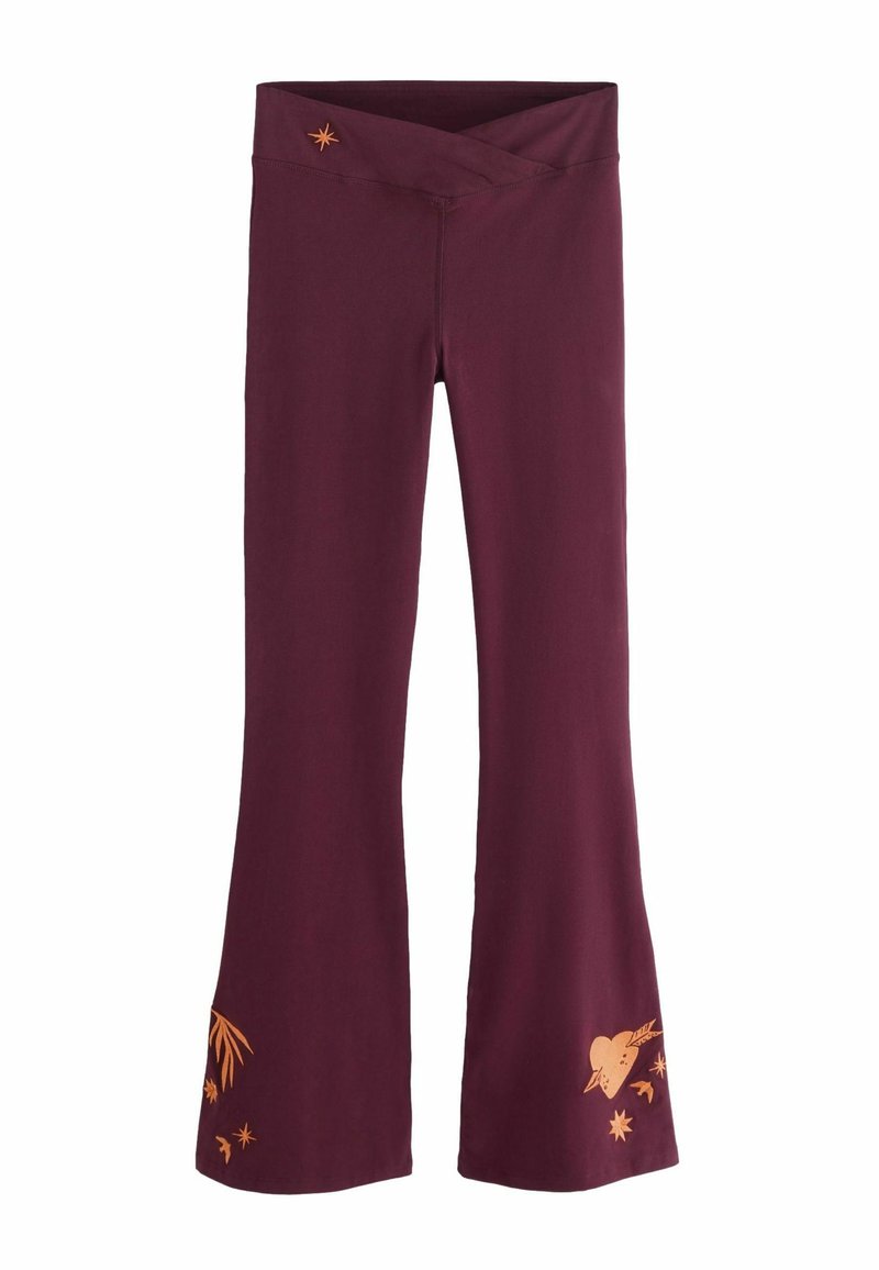 Marhuľovo červené rozšírené nohavice s prekríženým pásom a oranžovými grafickými detailmi, vrátane listov, sŕdc a hviezd pri leme.