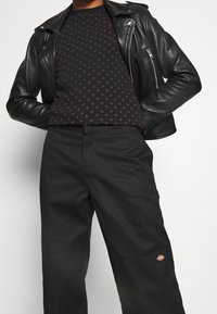 Black leather motorcycle jacket over a black shirt with a small burgundy dot pattern, paired with wide black trousers featuring a logo.