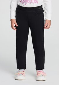 Leggings neri realizzati in tessuto elasticizzato, con due tasche frontali e una cintura liscia. Abbinati a scarpe bianche con cinturini color pastello.