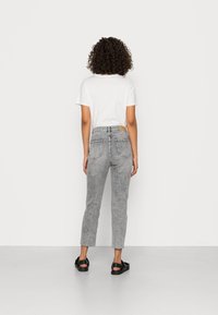 Grijze high-waisted jeans met een vervaagde textuur, vijf zakken en een rauwe zoom, gecombineerd met een effen wit t-shirt en zwarte sandalen.