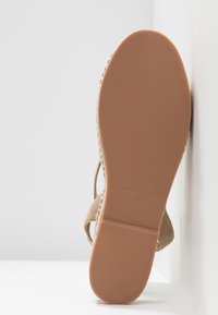 Semelle de sandale face vers l'avant avec un dessous lisse de couleur marron clair, indiquant la taille 37 et le texte « Fabriqué en Espagne ».