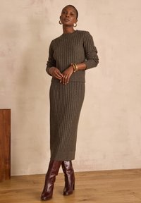 Ensemble en tricot côtelé vert foncé avec jupe assortie, fabriqué en tissu texturé avec des accents métalliques. Assorti à des bottes à talons bordeaux.