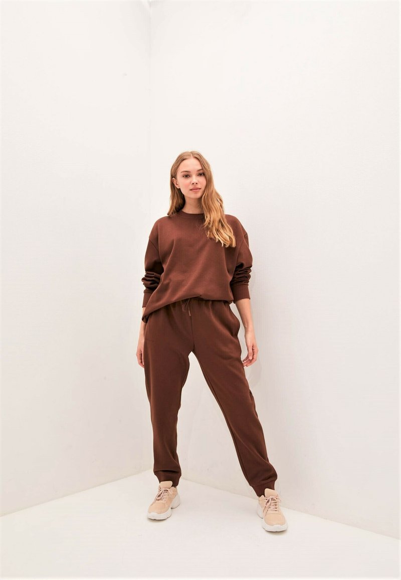 Brauner, kurzer Sweatshirt mit gerippten Bündchen, kombiniert mit passenden, hochgeschnittenen Jogginghosen, beide aus einem weichen, strukturierten Material.