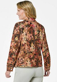 Denim jacket met bloemenpatroon in warme tonen van oranje, roze en bruin. Bevat een gestructureerd ontwerp met knoopaccenten en schoudernaden.