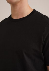 Camiseta de algodón negra con cuello redondo y mangas cortas. Textura suave, diseño ajustado con costuras mínimas y sin patrones ni acentos.