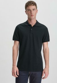 Black polo shirt made of textured cotton. Short sleeves, two-button placket, and subtle logo detail on the sleeve. Fitted design.