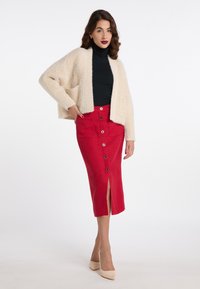 Cremefarvet, struktureret cardigan med åben front, parret med en tætsiddende rød nederdel med knapper og en frontslids, både elegant og moderne.