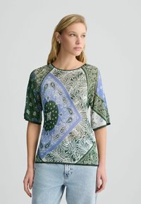 Mitmevärviline lühikeste varrukatega pluus, millel on segatud rohelise, sinise ja valge paisley ning zebra mustrid, ümmargune kaelus ja pehme kangas.
