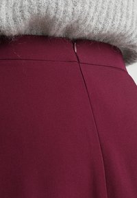 Burgunderrote Bleistiftrock aus glattem Stoff, mit einem versteckten Reißverschluss auf der Rückseite und einer taillierten Silhouette für einen maßgeschneiderten Look.