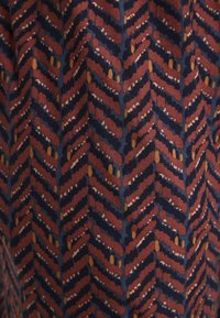 Gestreepte stof met een chevronontwerp in marineblauw, bordeauxrood en mosterdgeel, met een textuurafwerking en subtiele variaties in het patroon.