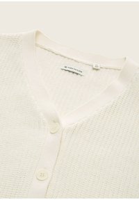 Weißer gestrickter Cardigan mit V-Ausschnitt, zwei vorderen Knöpfen und geripptem Saum. Das Etikett innen zeigt die Größe M (152) an. Die Textur ist weich und gewoben.