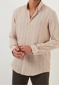 Světlobéžová košile na knoflíky s bílými vertikálními pruhy, vyrobená z texturované látky, s klasickým límcem a manžetami na knoflíky.