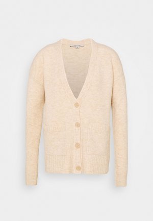 Cardigan en maille beige doux avec manches longues, encolure en V, quatre boutons devant et deux poches carrées sur un fond uni.