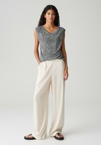 Zwart-wit gestreept mouwloos topje gecombineerd met crème wijde broek en zwarte slippers. Gladde stof met een ontspannen pasvorm.