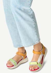 Multicolored sandals featuring a white, yellow, mint, and lavender design. The sole is thick, with a red accent and adjustable straps.