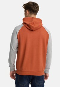 Hoodie met een oranje lijf en grijze raglanmouwen. Beschikt over een kangoeroezak, ribgebreide manchetten en een gestructureerde afwerking.