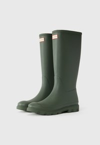 Green rubber rain boots with a curved shape and textured sole. Features a red and white logo on the upper side. Smooth, matte finish.