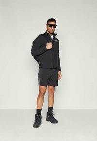 Czarna wodoodporna kurtka, pasujące szorty i buty turystyczne. W zestawie czarny plecak i ciemne okulary przeciwsłoneczne. Prosty design i funkcjonalny styl.