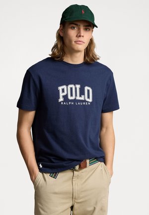 Navy blue cotton t-shirt with "POLO RALPH LAUREN" printed in white, paired with khaki pants and a green cap featuring a logo.