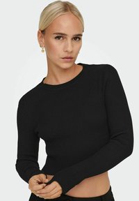 Crop top a maniche lunghe nero a coste con scollatura rotonda e silhouette aderente. Il materiale ha una finitura texturizzata.