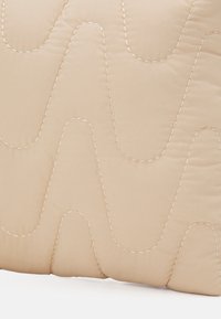 Cuscino color beige trapuntato con motivo a onde e cuciture a contrasto. Texture liscia con bordi arrotondati, che enfatizzano i contorni morbidi.